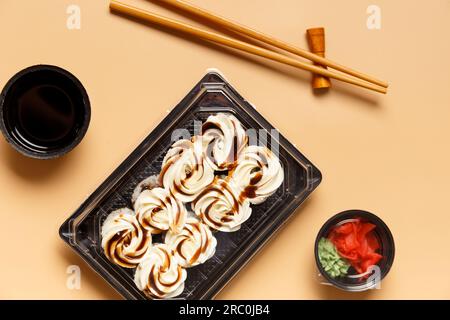 Rouleaux de sushi au saumon, garnis de fromage à la crème et sauce dans un emballage en plastique, baguettes, gingembre, sauce sur fond clair. Banque D'Images