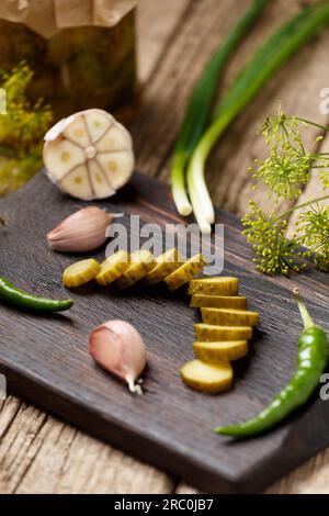 Concombre en conserve mariné tranché sur une planche à découper en bois foncé, ail frais, piments forts, oignons verts sur un fond en bois. Nature morte de légume Banque D'Images