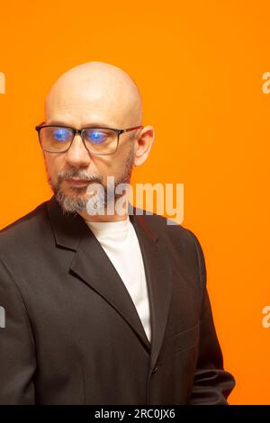 Homme élégant dans une veste de costume, barbu, chauve et portant des lunettes. Isolé sur fond orange Banque D'Images