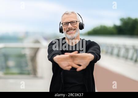 Heureux joyeux sportif retraité mature faisant des exercices d'étirement des bras Banque D'Images