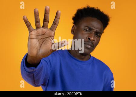 Triste déçu jeune homme noir montrant geste d'arrêt, fond jaune Banque D'Images