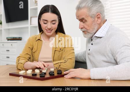 Jouer aux dames. Homme senior apprenant jeune femme à table dans la salle Banque D'Images