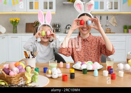 Mère et sa fille mignonne couvrant les yeux avec des œufs de Pâques magnifiquement peints à table dans la cuisine Banque D'Images