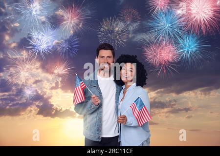 4 juillet - jour de l'indépendance de l'Amérique. Heureux couple tenant les drapeaux nationaux des États-Unis contre le ciel avec des feux d'artifice Banque D'Images