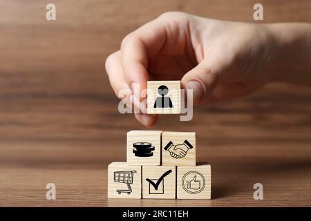 Acheteur professionnel. Femme construisant pyramide de cubes avec différentes icônes sur fond en bois, closeup Banque D'Images