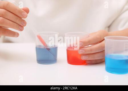 Fille mélangeant des liquides colorés à la table blanche à l'intérieur, gros plan. Kit d'expérimentation chimique pour enfants Banque D'Images