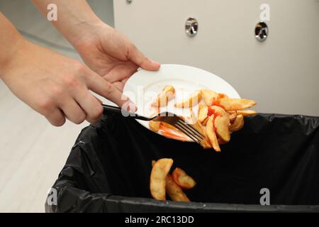 Femme jetant des pommes de terre cuites avec du ketchup dans la poubelle à l'intérieur, gros plan Banque D'Images