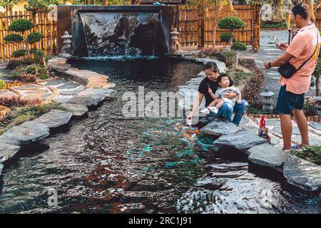 KANCHANABURI -THAÏLANDE, 30 MARS 2023 : touristes non identifiés viennent visiter et nourrir koi ou carpe fantaisie dans un petit étang avec beau jardin décoré Banque D'Images