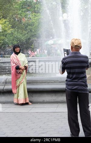 Une femme musulmane en robe ethnique traditionnelle et probablement un touriste pose pour des photos près de la fontaine dans Washington Square Park à Manhattan, New York. Banque D'Images