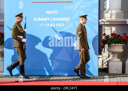 Vilnius, Lituanie. 11 juillet 2023. Des soldats marchent devant un panneau pendant le sommet de haut niveau de l'OTAN. Le Président de la Lituanie organise le dîner des dirigeants mondiaux au Palais présidentiel. L'ordre du jour du sommet couvre la candidature de l'Ukraine à l'adhésion à l'organisation, le processus d'adhésion de la Suède, l'augmentation des stocks d'armes et la révision des plans. Crédit : SOPA Images Limited/Alamy Live News Banque D'Images