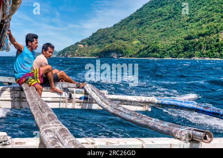 Île de Mindoro, Philippines - 29 février 2020. Deux membres d'équipage philippins sont assis sur les stabilisateurs en bois et en bambou d'un passager traditionnel bangka A. Banque D'Images