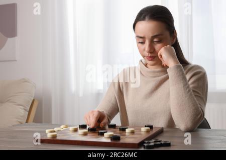 Jouer aux dames. Femme concentrée pensant au prochain mouvement à table dans la salle, espace pour le texte Banque D'Images