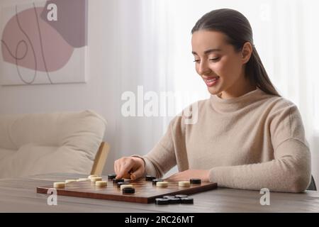 Jouer aux dames. Jeune femme pensant au prochain mouvement à table dans la salle, espace pour le texte Banque D'Images