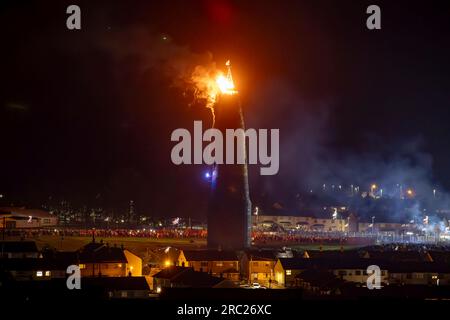 Les gens regardent l'incendie du feu de joie loyaliste de Craigyhill à Larne, Co Antrim, la onzième nuit. Inaugurant les douzième commémorations. Date de la photo : mardi 11 juillet 2023. Banque D'Images