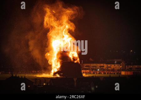 Les gens regardent l'incendie du feu de joie loyaliste de Craigyhill à Larne, Co Antrim, la onzième nuit. Inaugurant les douzième commémorations. Date de la photo : mercredi 12 juillet 2023. Banque D'Images