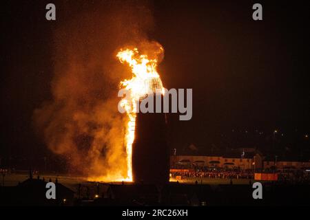 Les gens regardent l'incendie du feu de joie loyaliste de Craigyhill à Larne, Co Antrim, la onzième nuit. Inaugurant les douzième commémorations. Date de la photo : mercredi 12 juillet 2023. Banque D'Images