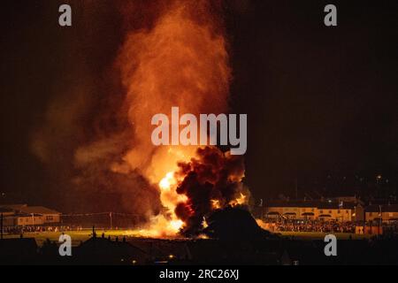 Les gens regardent l'incendie du feu de joie loyaliste de Craigyhill à Larne, Co Antrim, la onzième nuit. Inaugurant les douzième commémorations. Date de la photo : mercredi 12 juillet 2023. Banque D'Images