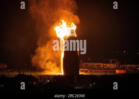 Les gens regardent l'incendie du feu de joie loyaliste de Craigyhill à Larne, Co Antrim, la onzième nuit. Inaugurant les douzième commémorations. Date de la photo : mercredi 12 juillet 2023. Banque D'Images