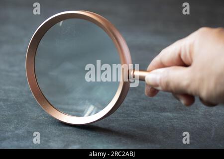 Main tenant une loupe sur fond bleu.espace de copie. Banque D'Images