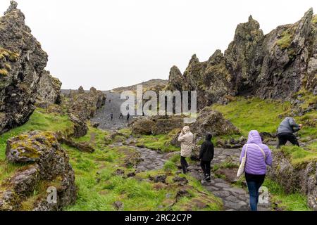 Les gens marchent sur un chemin entre les montagnes volcaniques jusqu'à la plage de sable noir de Djupalonssandur en Islande Banque D'Images