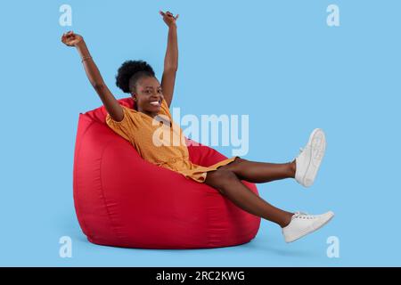 Belle jeune femme assise sur la chaise Beanbag sur fond bleu clair Banque D'Images