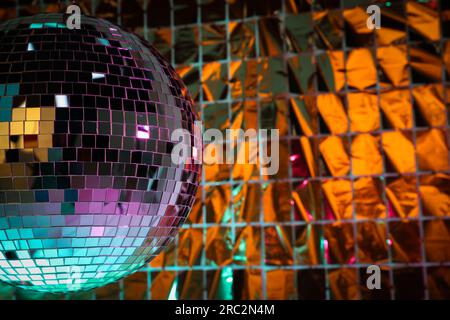 Boule disco brillante contre rideau de fête en aluminium sous la lumière turquoise et orange, espace pour le texte Banque D'Images