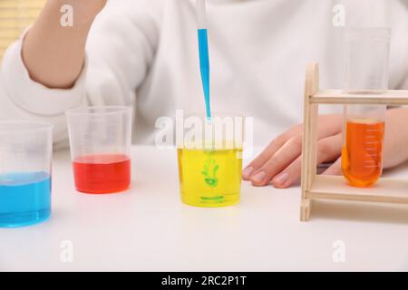 Fille mélangeant des liquides colorés à la table blanche à l'intérieur, gros plan. Kit d'expérimentation chimique pour enfants Banque D'Images