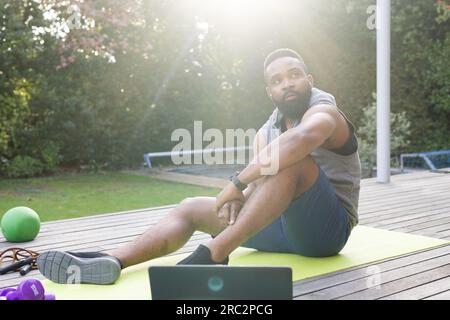 Homme afro-américain réfléchi avec ordinateur portable assis sur le tapis dans le jardin Banque D'Images