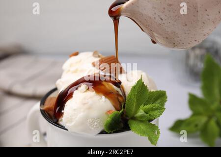 Verser la sauce caramel sur la crème glacée avec des bonbons et des feuilles de menthe, gros plan Banque D'Images