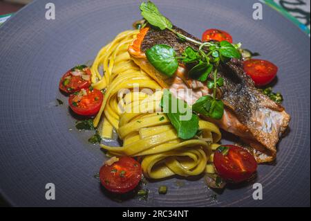 Nourriture dans l'assiette. Saumon grillé, pâtes, tomote et salade. Délicieux. Banque D'Images