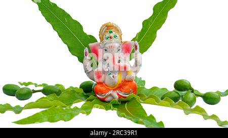 Seigneur Ganesha petite idole pooja prière à la maison avec des feuilles d'ashoka et des fruits verts décor de fond. Banque D'Images