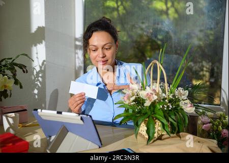 Jolie femme fleuriste recevant l'ordre pour arrangement floral, discutant avec les clients via la conférence en ligne la conception de bouquet, travaillant en floral Banque D'Images