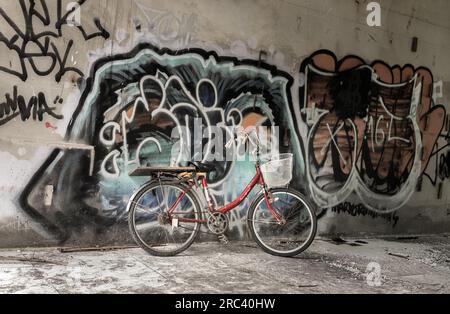 Bangkok, Thaïlande - 08 juillet 2023 - Un vélo rouge est garé à côté des motifs de graffiti sur le mur, dans le bâtiment abandonné. Espace pour le texte Banque D'Images