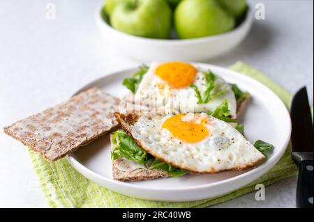 Assiette de petit déjeuner sans gluten et végétarien avec du pain de Cripbread à faible teneur en glucides, roquette, œufs au plat et pommes vertes sur fond blanc Banque D'Images