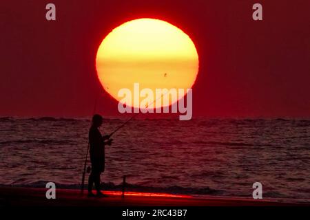 Île de Palms, États-Unis. 12 juillet 2023. Une silhouette de pêcheur face à un lever de soleil dramatique apparaissant comme une boule géante au-dessus de la plage, le 12 juillet 2023 à Isle of Palms, Caroline du Sud. Une vague de chaleur prolongée dans le sud des États-Unis continue d'apporter un temps extrêmement chaud et humide à la région. Crédit : Richard Ellis/Richard Ellis/Alamy Live News Banque D'Images