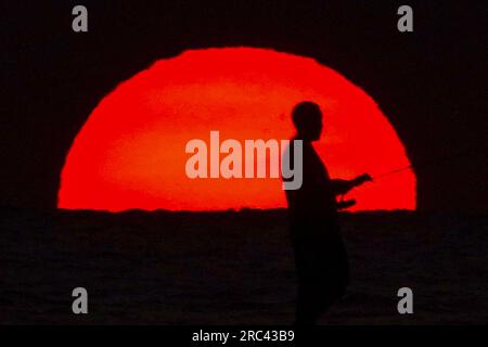 Île de Palms, États-Unis. 12 juillet 2023. Une silhouette de pêcheur face à un lever de soleil dramatique apparaissant comme une boule géante au-dessus de la plage, le 12 juillet 2023 à Isle of Palms, Caroline du Sud. Une vague de chaleur prolongée dans le sud des États-Unis continue d'apporter un temps extrêmement chaud et humide à la région. Crédit : Richard Ellis/Richard Ellis/Alamy Live News Banque D'Images