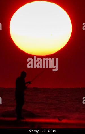 Île de Palms, États-Unis. 12 juillet 2023. Une silhouette de pêcheur face à un lever de soleil dramatique apparaissant comme une boule géante au-dessus de la plage, le 12 juillet 2023 à Isle of Palms, Caroline du Sud. Une vague de chaleur prolongée dans le sud des États-Unis continue d'apporter un temps extrêmement chaud et humide à la région. Crédit : Richard Ellis/Richard Ellis/Alamy Live News Banque D'Images