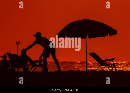 Île de Palms, États-Unis. 12 juillet 2023. Un travailleur de station se déforme par le lever du soleil alors qu'il installe des chaises de plage et un parasol au Wild Dunes Resort, le 12 juillet 2023 à Isle of Palms, Caroline du Sud. Une vague de chaleur prolongée dans le sud des États-Unis continue d'apporter un temps extrêmement chaud et humide à la région. Crédit : Richard Ellis/Richard Ellis/Alamy Live News Banque D'Images