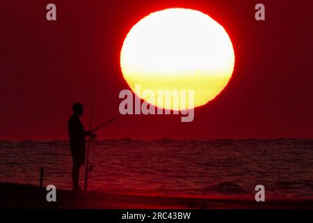 Île de Palms, États-Unis. 12 juillet 2023. Une silhouette de pêcheur face à un lever de soleil dramatique apparaissant comme une boule géante au-dessus de la plage, le 12 juillet 2023 à Isle of Palms, Caroline du Sud. Une vague de chaleur prolongée dans le sud des États-Unis continue d'apporter un temps extrêmement chaud et humide à la région. Crédit : Richard Ellis/Richard Ellis/Alamy Live News Banque D'Images