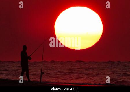 Île de Palms, États-Unis. 12 juillet 2023. Une silhouette de pêcheur face à un lever de soleil dramatique apparaissant comme une boule géante au-dessus de la plage, le 12 juillet 2023 à Isle of Palms, Caroline du Sud. Une vague de chaleur prolongée dans le sud des États-Unis continue d'apporter un temps extrêmement chaud et humide à la région. Crédit : Richard Ellis/Richard Ellis/Alamy Live News Banque D'Images