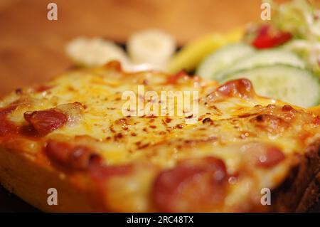 Pain grillé au fromage avec saucisse, bacon et salade de concombre Banque D'Images