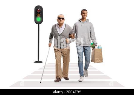 Jeune homme afro-américain avec des sacs d'épicerie marchant avec un homme aveugle âgé à un passage pour piétons isolé sur fond blanc Banque D'Images