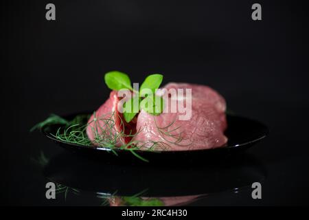 un morceau de viande de porc fraîche dans une assiette, isolé sur fond noir. Banque D'Images