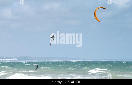 Brighton Royaume-Uni 12 juillet 2023 - les kitesurfers profitent des conditions aérées au large de la plage de Lancing, près de Brighton, que l'on peut voir au loin alors que le temps instable devrait se répandre à travers la Grande-Bretagne dans les prochains jours : Credit Simon Dack / Alamy Live News Banque D'Images