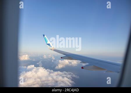 Aile d'un avion volant dans le ciel bleu avec des nuages blancs. Banque D'Images