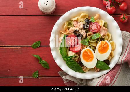 Salade de pâtes italiennes. Pâtes d'orecchiette au thon, à la tomate, à la cerise, à l'olive, au basilic et au parmesan sur fond rouge de table rustique ancienne. Traditi Banque D'Images