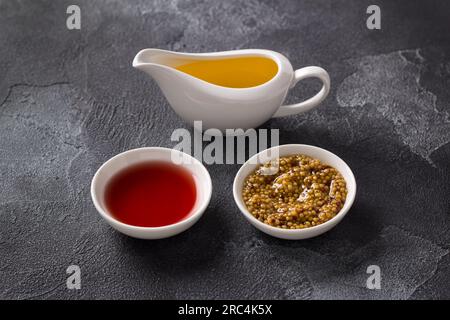 Vinaigre de vin, moutarde aux grains, huile végétale sur fond texturé foncé. Sauce vinaigrette Ingrédients. Banque D'Images
