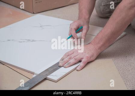 Les mains d'un homme marquant les carreaux de sol en céramique avec une règle et un crayon pour poser sur le sol. Mise au point sélective. Mise au point douce Banque D'Images