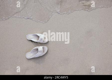 Vue de dessus des élégantes tongs blanches placées sur la plage de sable près de la mer pendant les vacances d'été sur les îles Baléares Banque D'Images