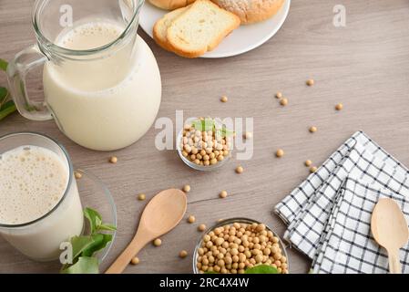 Lait de soja dans un verre et une cruche pour le petit déjeuner alternatif avec des bols pleins de soja sur la table en bois avec des pâtisseries. Vue de dessus. Banque D'Images